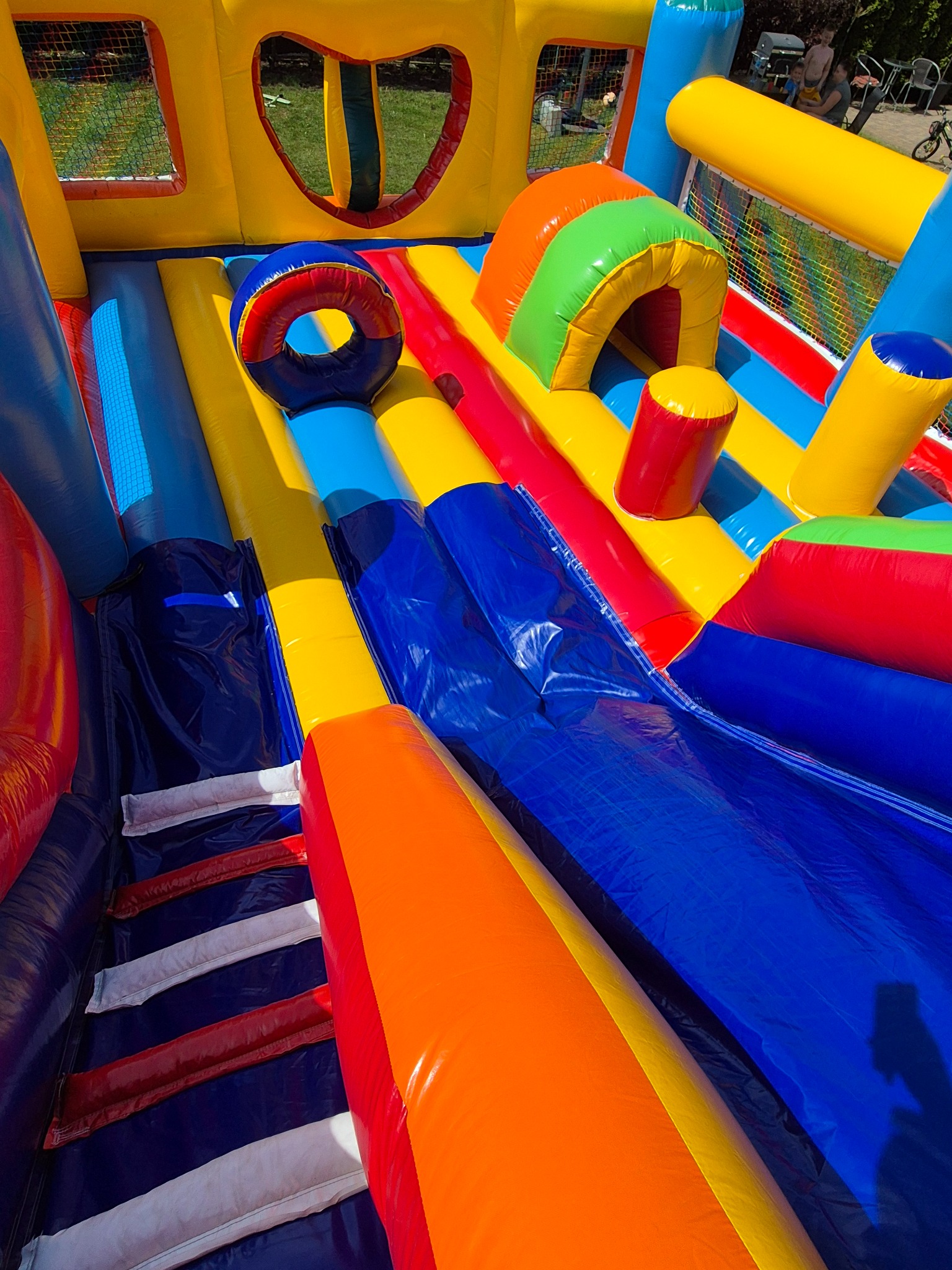 Wnętrze kolorowego dmuchańca z tunelem, przeszkodami i oknami z siatki, widok z góry, intensywne kolory.