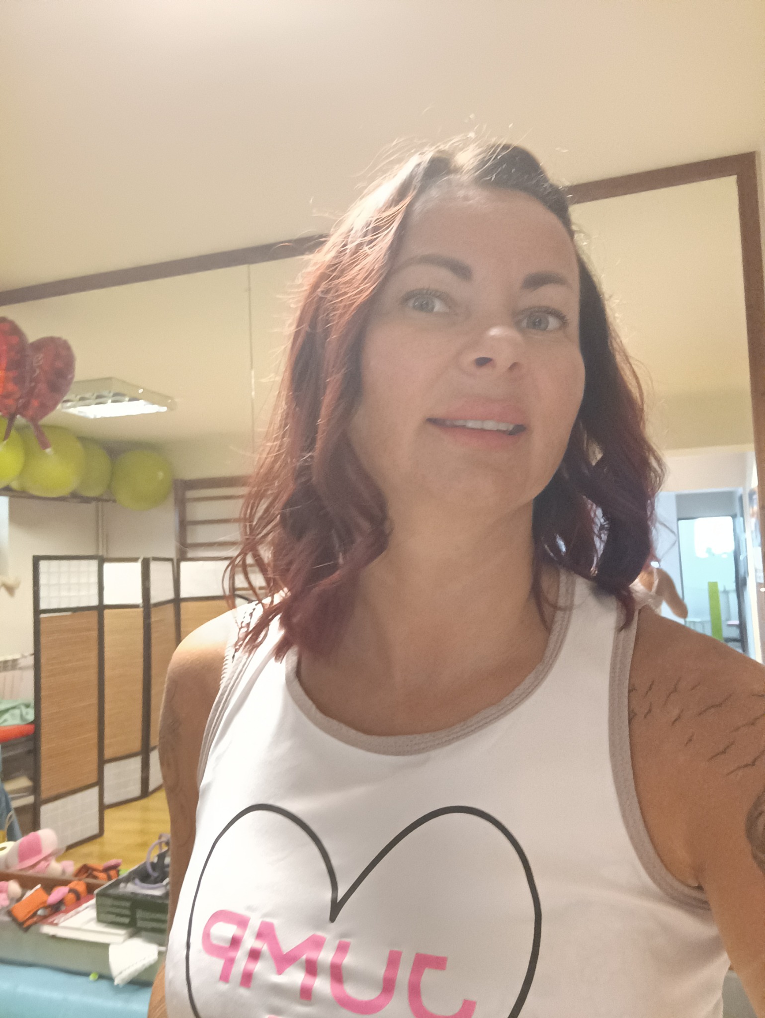 Kobieta z tatuażem na ramieniu robi selfie w gabinecie z piłkami do ćwiczeń i parawanem.