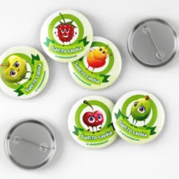 Zestaw okrągłych przypinek z grafikami owoców (malina, jabłko, gruszka, wiśnia, agrest) w stylu cartoon, z napisem 'Święto Sadów w Wierzchowicach', widoczne także metalowe elementy mocujące.