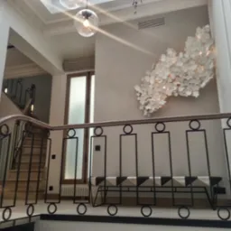 Nowoczesne wnętrze z czarno-białą ławką, dekoracją ścienną z białych kwiat&oacute;w i schodami w tle, oświetlone wiszącymi lampami.