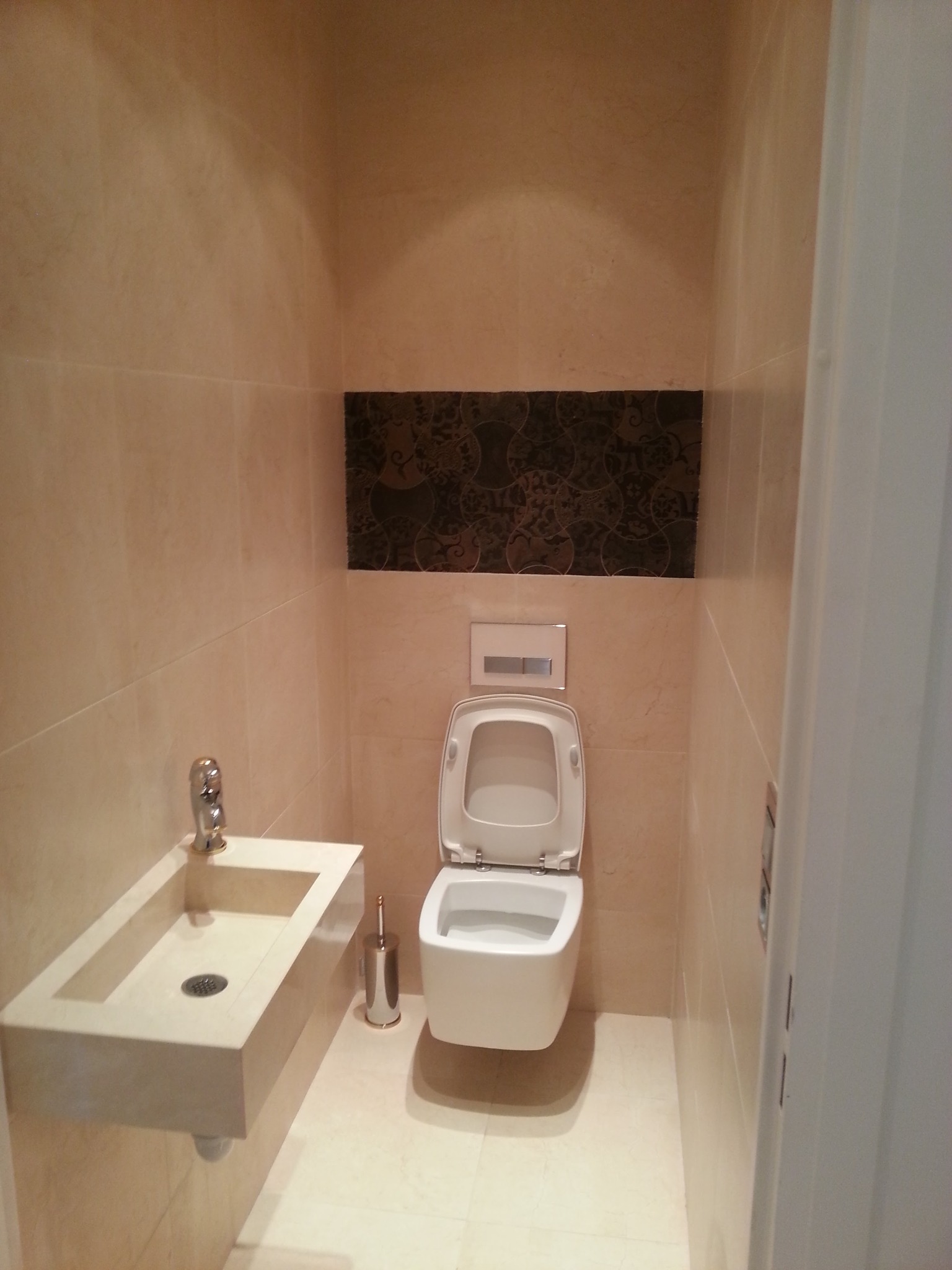 Nowoczesna łazienka z beżowymi płytkami, wiszącą toaletą i umywalką wpuszczaną w blat z tego samego materiału, akcentowana ciemnym pasem dekoracyjnym nad toaletą.