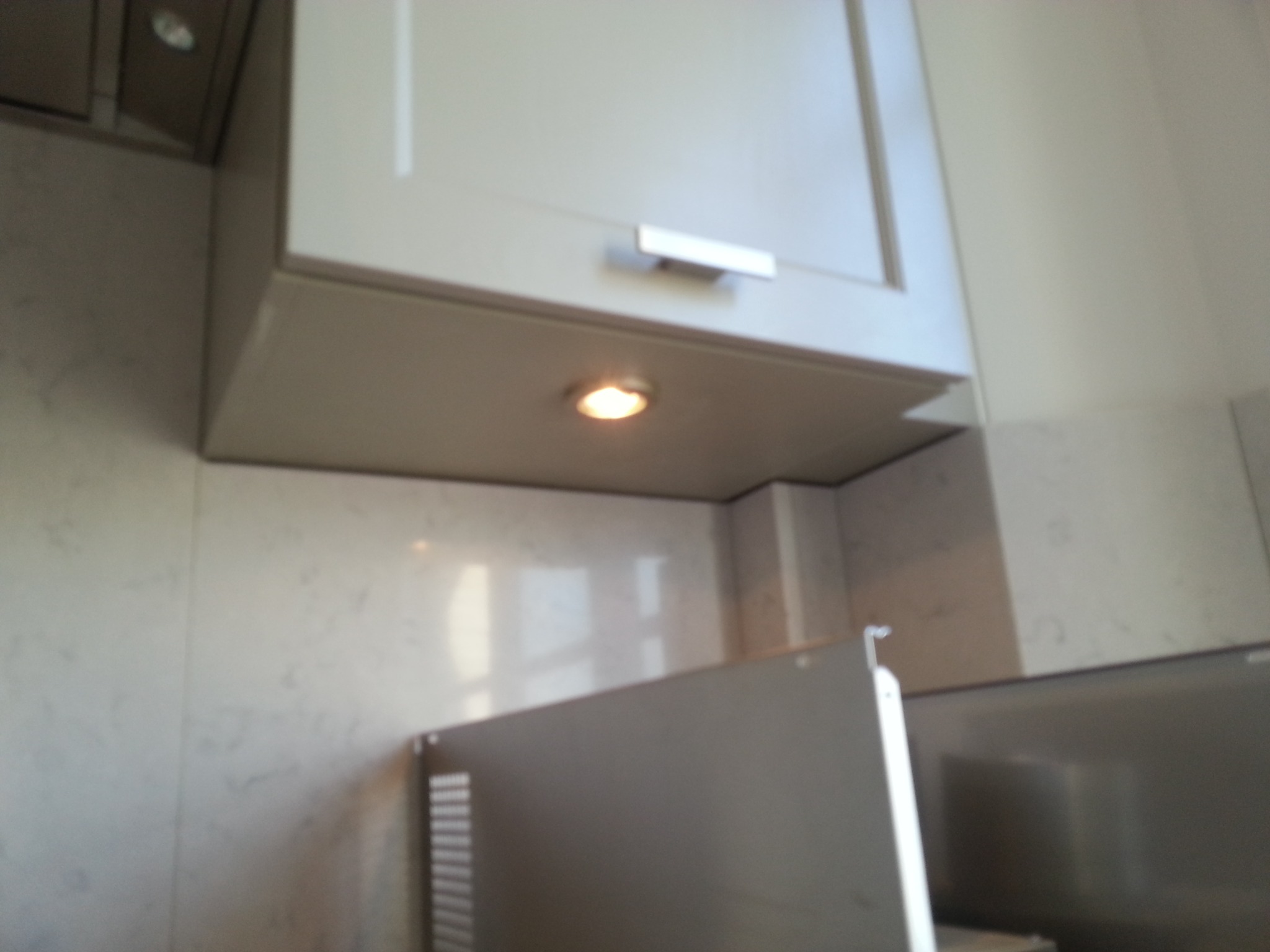 Zamontowana szafka kuchenna z oświetleniem punktowym LED pod spodem i marmurową płytą ścienną w tle.