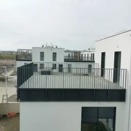 Nowoczesne, białe budynki z balkonami z czarną balustradą w minimalistycznym stylu. Widok z góry na osiedle w trakcie budowy.