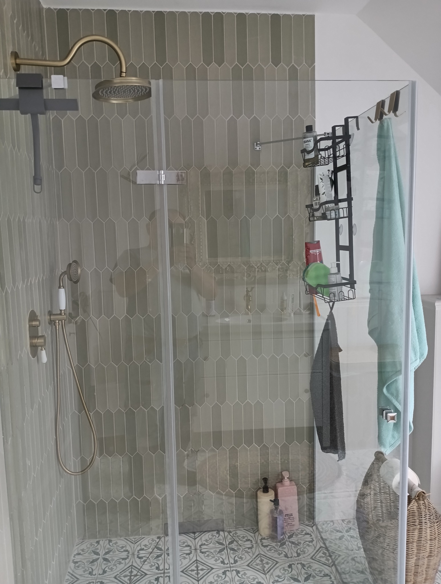 Szczegółowe ujęcie kabiny prysznicowej z armaturą w odcieniach złota i szaro-zielonymi, podłużnymi płytkami. Na podłodze wzorzyste płytki.