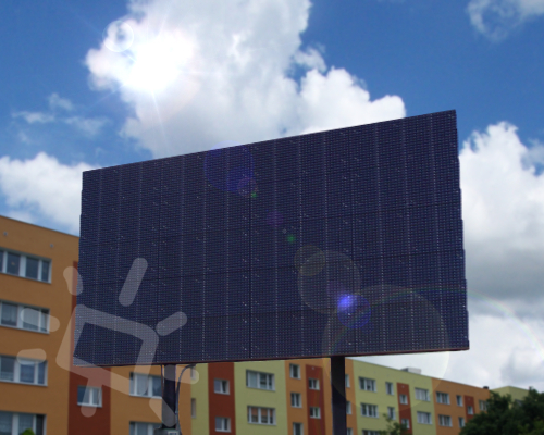 Prostokątny, ciemny ekran LED na tle błękitnego nieba z chmurami i budynków mieszkalnych.