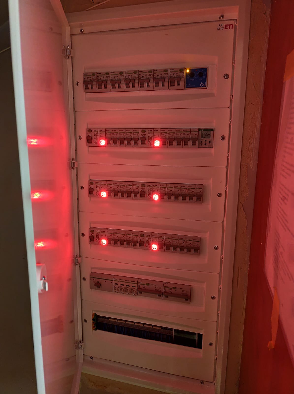 Otwarta skrzynka elektryczna ETI z wyłącznikami, niektóre z czerwonymi diodami, oświetlona czerwonym światłem