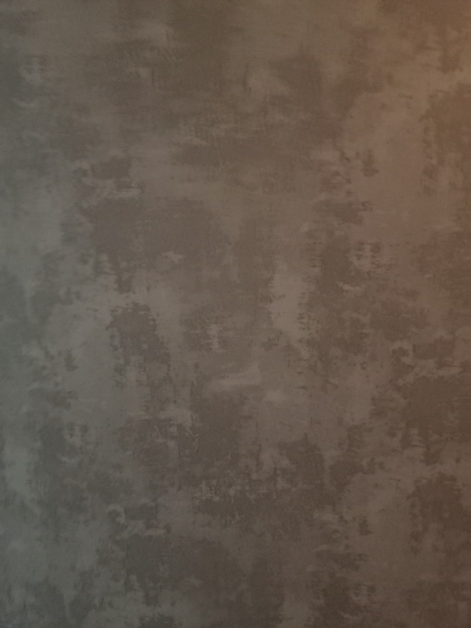 Szara ściana z efektem dekoracyjnym, imitującym przecierki i nieregularną fakturę, oświetlona z prawej strony.