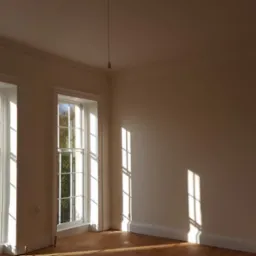 Pomalowane na jasny kolor wnętrze pokoju z parkietem i dwoma oknami w Jastrowiu, promienie słoneczne wpadają do środka.