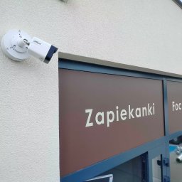 IntKaM System - Kamera Dahua zamontowana na elewacji budynku z szyldem 'Zapiekanki'. Zabezpieczenie lokalu gastronomicznego systemem monitoringu.