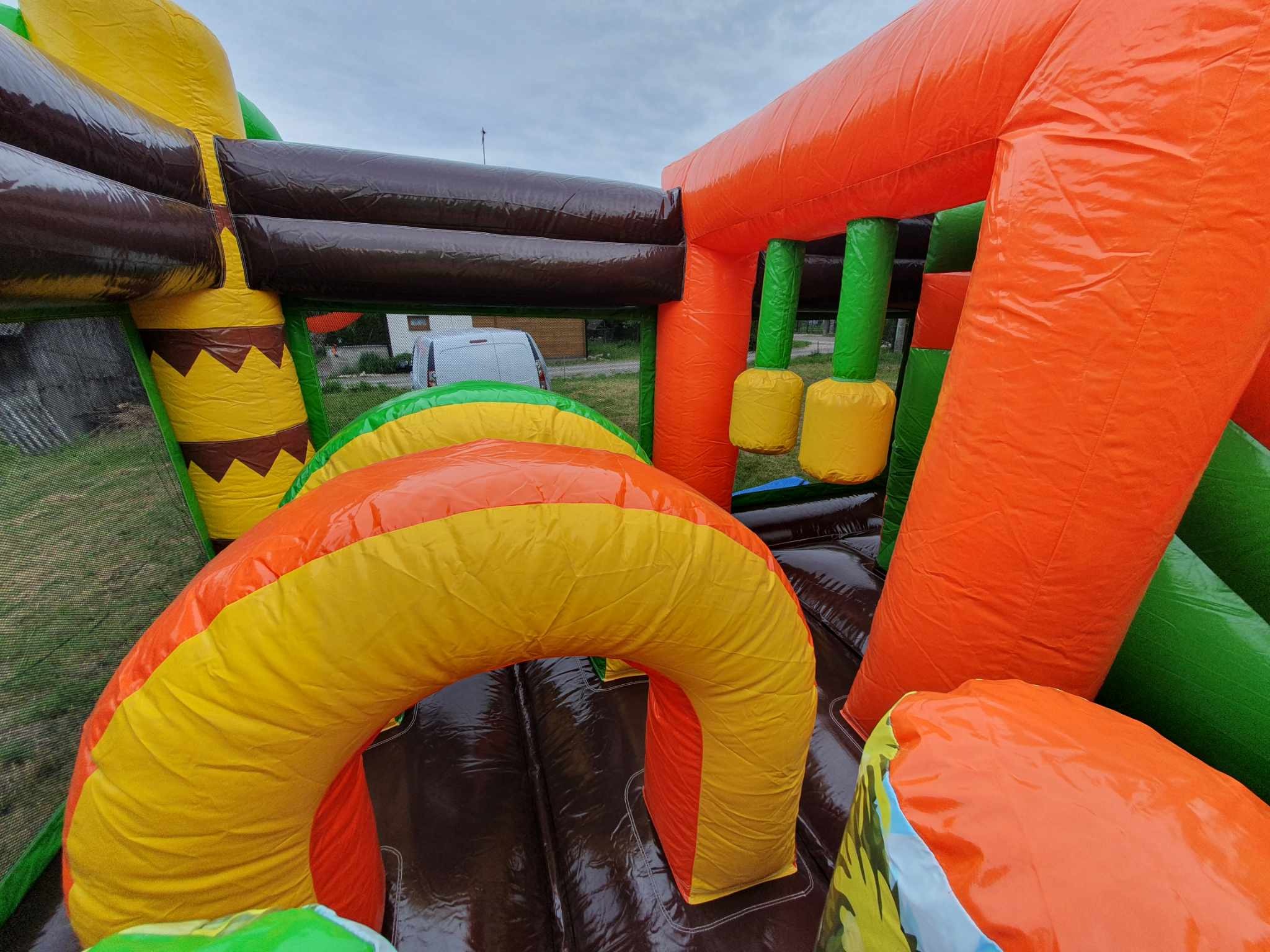 Kolorowy, dmuchany plac zabaw Dino w Bratkowicach z tunelem i przeszkodami, widok z wnętrza konstrukcji. Intensywne barwy, częściowo widoczny budynek w tle.