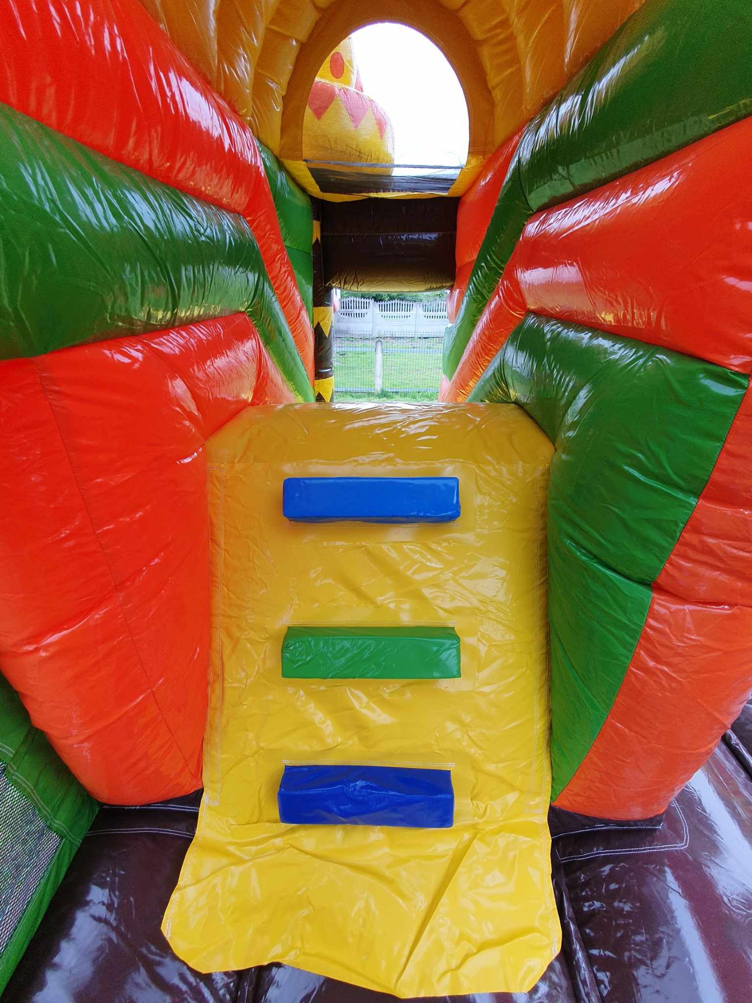 Wnętrze dmuchanego placu zabaw z żółtą ścianką wspinaczkową i kolorowymi elementami: czerwonymi, zielonymi i pomarańczowymi. Widok z dołu na górę.