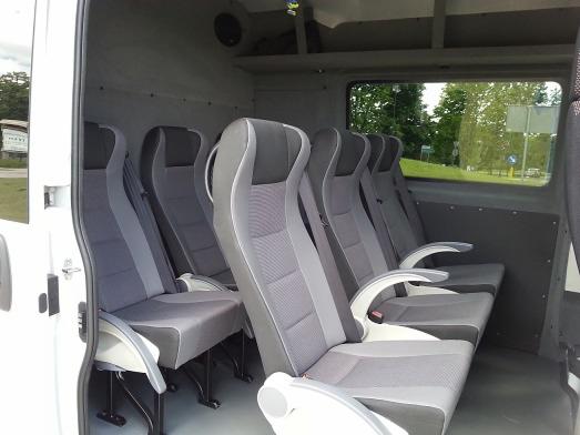 Wnętrze busa z rzędem szarych foteli z podłokietnikami, widok z boku, jasne wnętrze, okno z widokiem na zewnątrz.