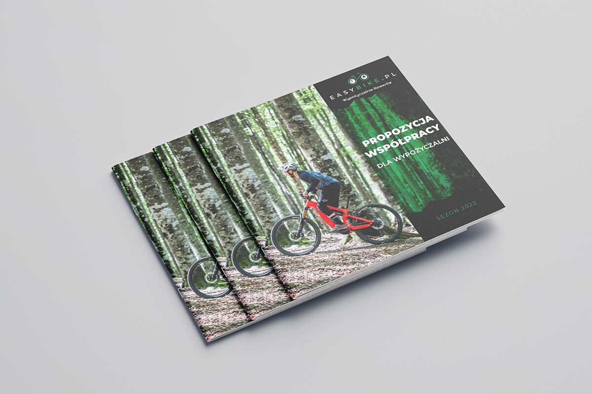 Stos ulotek reklamowych z rowerzystą na tle leśnym, promujących współpracę z wypożyczalnią rowerów EasyBike.pl, sezon 2022.
