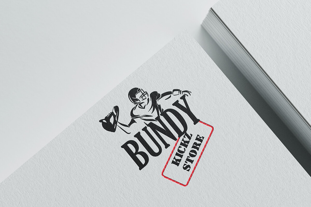 Czarno-białe logo przedstawiające gracza futbolu amerykańskiego rzucającego butem, obok nazwy 'BUNDY KICKZ STORE' w czerwonej ramce, umieszczone na białym papierze z plikiem kartek w tle.