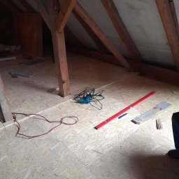 Adrian Sosna firma ogólnobudowlana - Poddasze w trakcie prac adaptacyjnych: surowa drewniana konstrukcja, płyty OSB na podłodze, poziomica, wiertarka i narzędzia przygotowane do dalszych prac wykończeniowych.