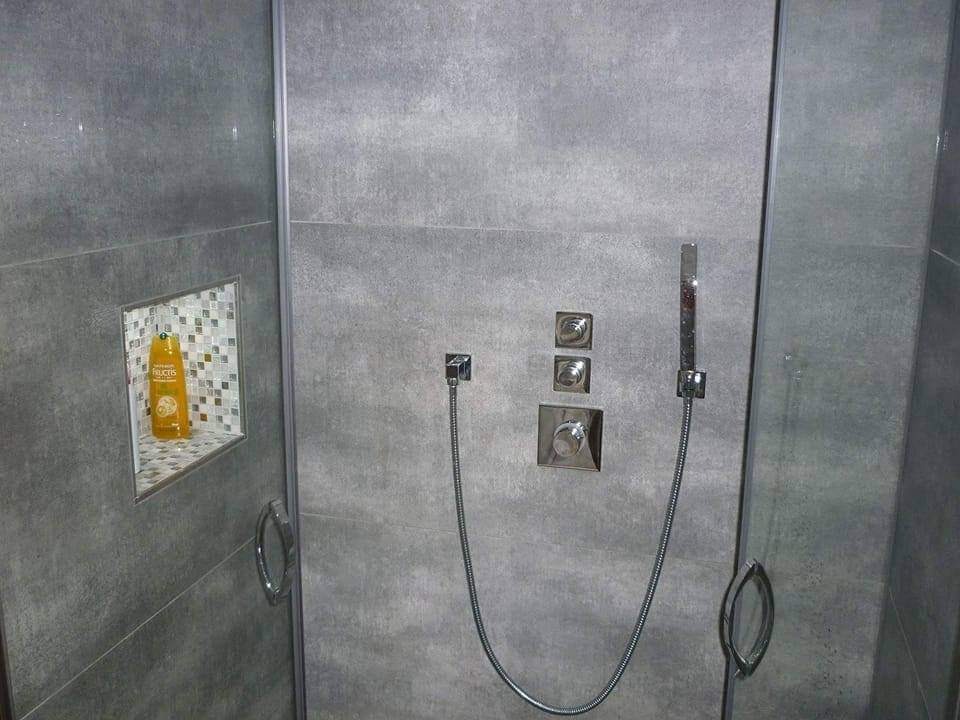 Szara kabina prysznicowa z mozaiką w niszy na kosmetyki, nowoczesna bateria i deszczownica.