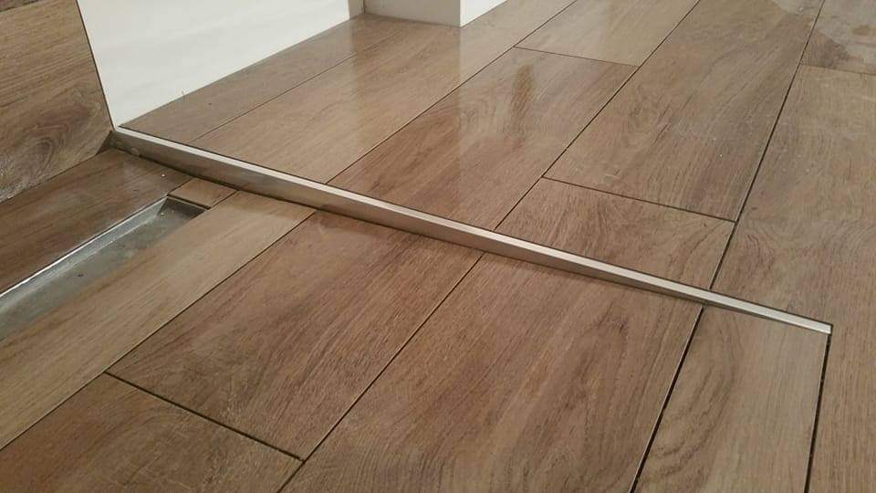 Ułożona podłoga z płytek imitujących drewno, z widocznym odpływem liniowym przy ścianie i listwą progową.