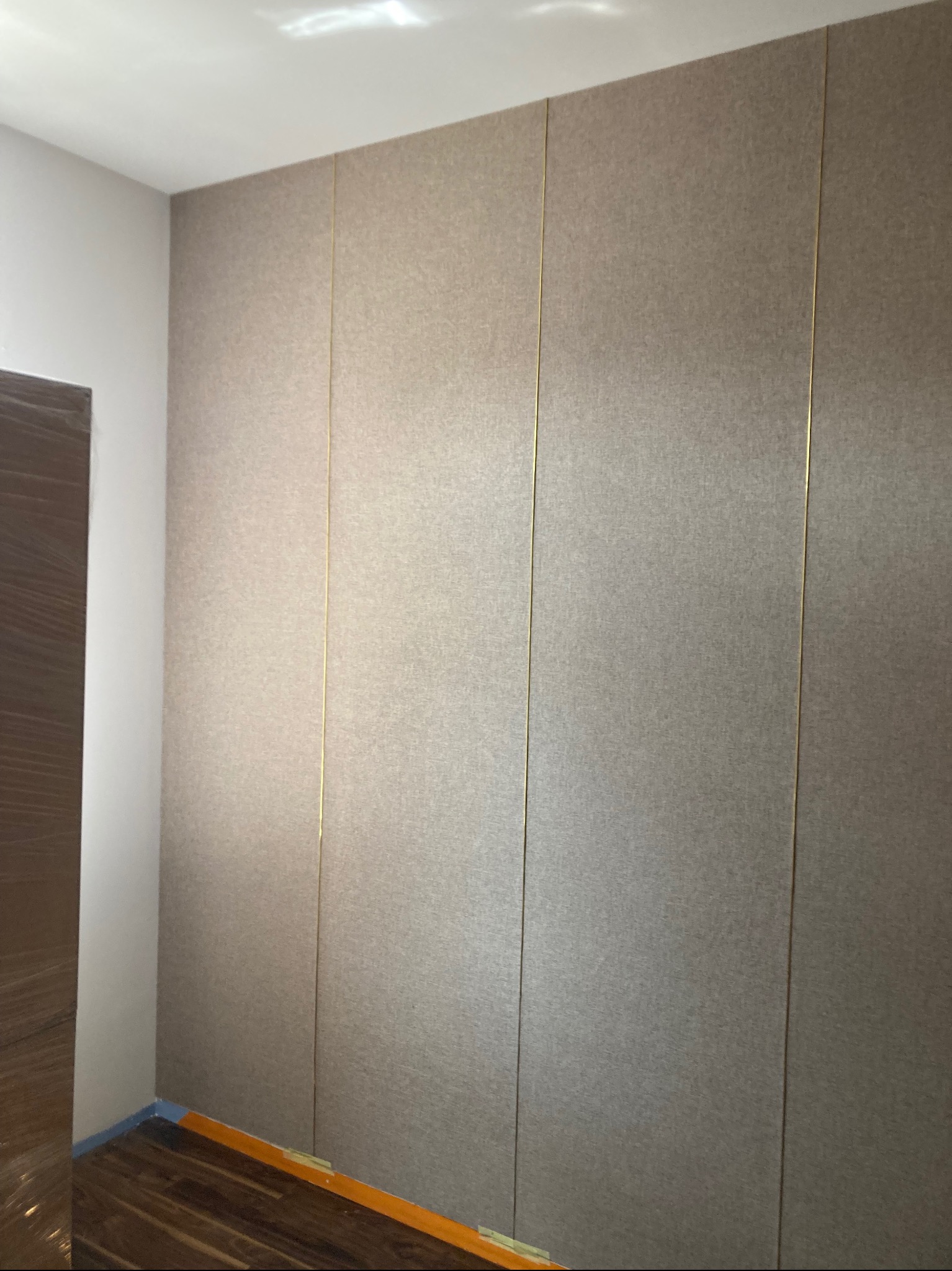 Beżowa ściana wykończona panelami z delikatną złotą listwą oddzielającą, widoczny fragment drewnianej podłogi i biała ściana boczna.