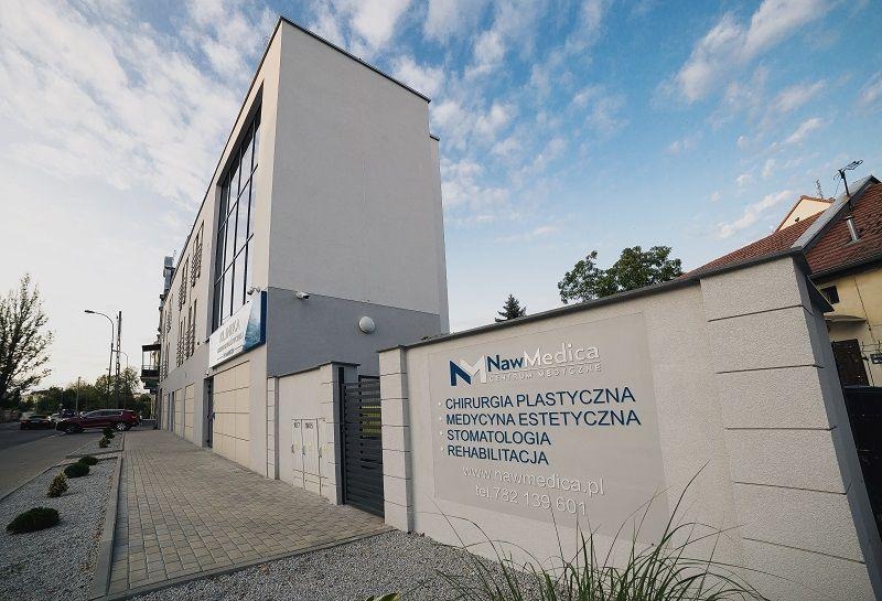 Nowoczesny budynek centrum medycznego NawMedica z tablicą informacyjną, na której wymienione są świadczone usługi: chirurgia plastyczna, medycyna estetyczna, stomatologia i rehabilitacja.