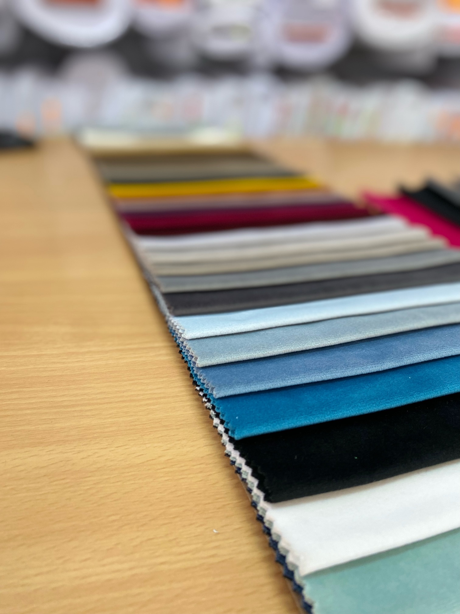 Próbki tkanin w różnych odcieniach ułożone rzędami na drewnianym blacie, prezentujące szeroką gamę kolorystyczną i fakturę materiałów.