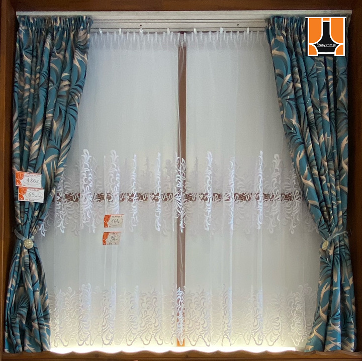 Okno z firanką z białym haftem i zasłonami w turkusowe liście, upięte sznurkiem z ozdobnym guzikiem, widoczne metki z cenami.