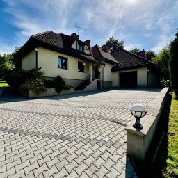 4Invest - Dwupiętrowy dom jednorodzinny z garażem, widoczny z perspektywy podjazdu wyłożonego szarą kostką brukową, oświetlonego kulistą lampą ogrodową.