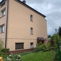 4Invest - Widok z poziomu ogrodu na trzypiętrowy budynek z beżową elewacją, brązowymi oknami i dachem, oraz zadbanym trawnikiem i rabatami kwiatowymi w odcieniach czerwieni, żółci, fioletu i bieli.