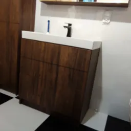 Nowoczesna łazienka z drewnianą szafką pod umywalkę z trzema szufladami, drewnianą ścianą z boazerią, białą umywalką z czarną baterią, toaletą i podłogą w szachownicę.