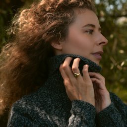 Joanna Tołwińska Fotografka - Portret kobiety z profilu, kręcone włosy, szary sweter z golfem, złoty pierścionek z zielonym oczkiem, naturalne światło.