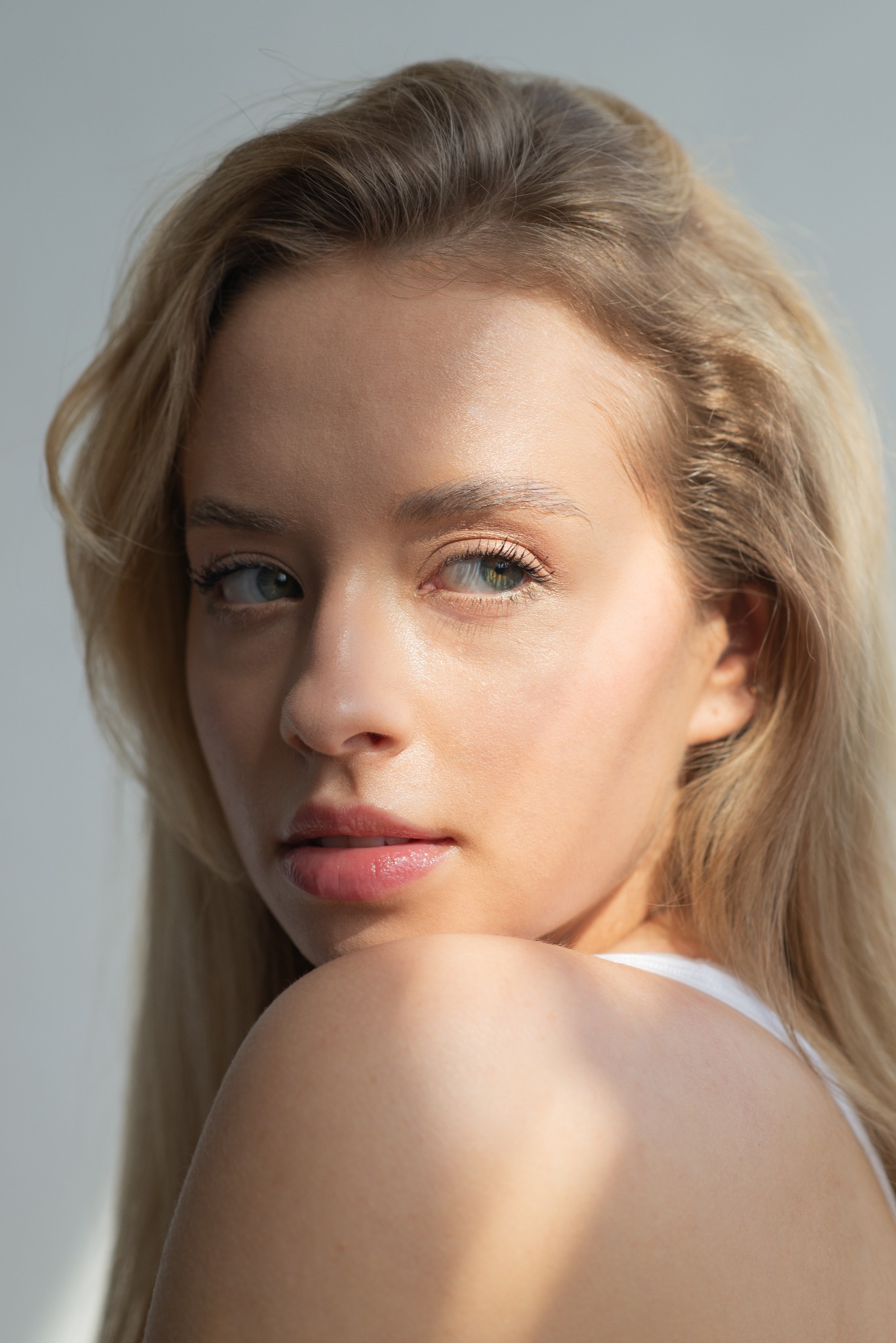 Portret młodej kobiety o jasnych włosach i intensywnym spojrzeniu, oświetlonej naturalnym światłem, z delikatnym makijażem.