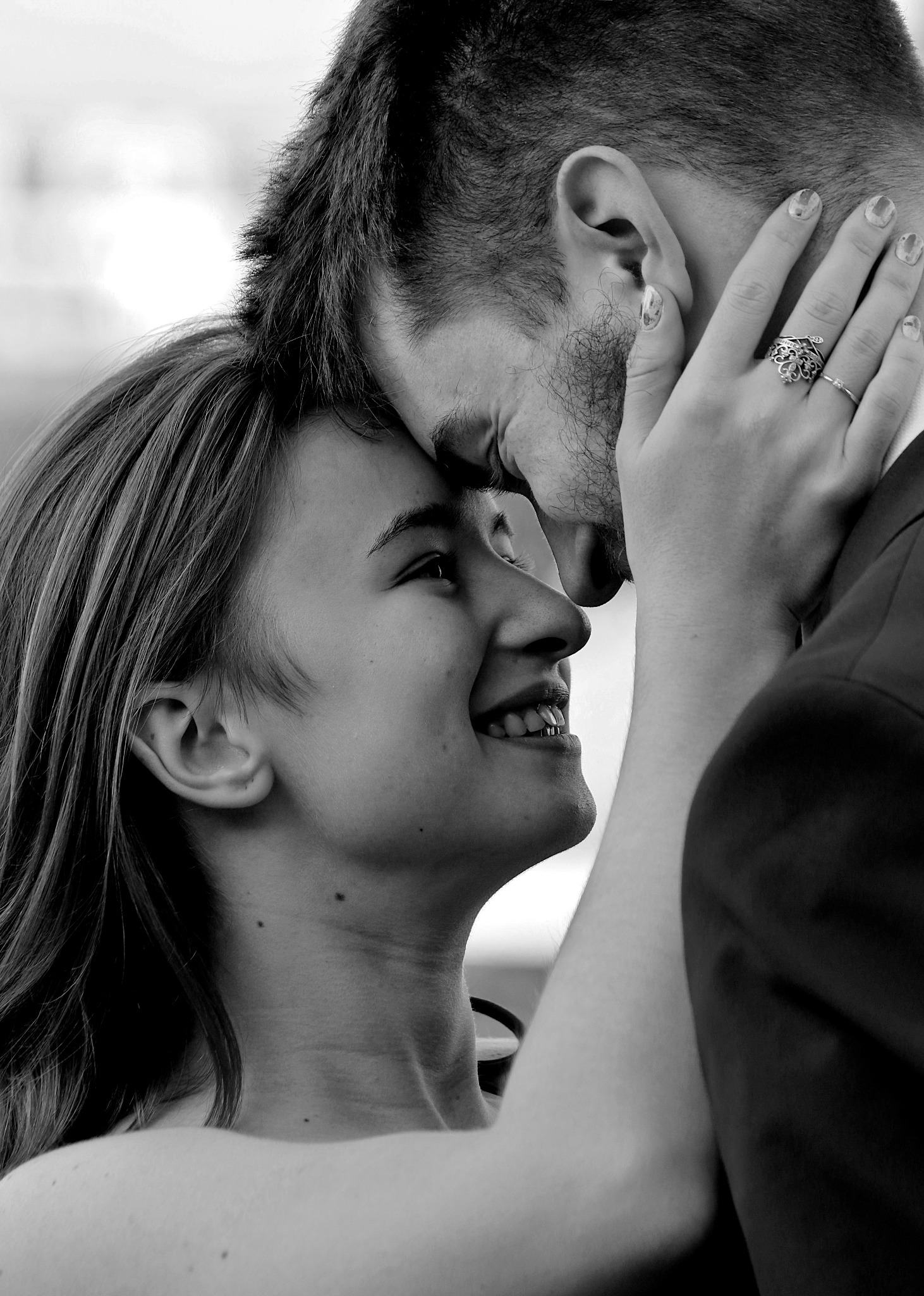 Czarno-białe zbliżenie szczęśliwej pary dotykającej się czołami, kobieta uśmiecha się patrząc w górę, pierścionek na jej palcu.