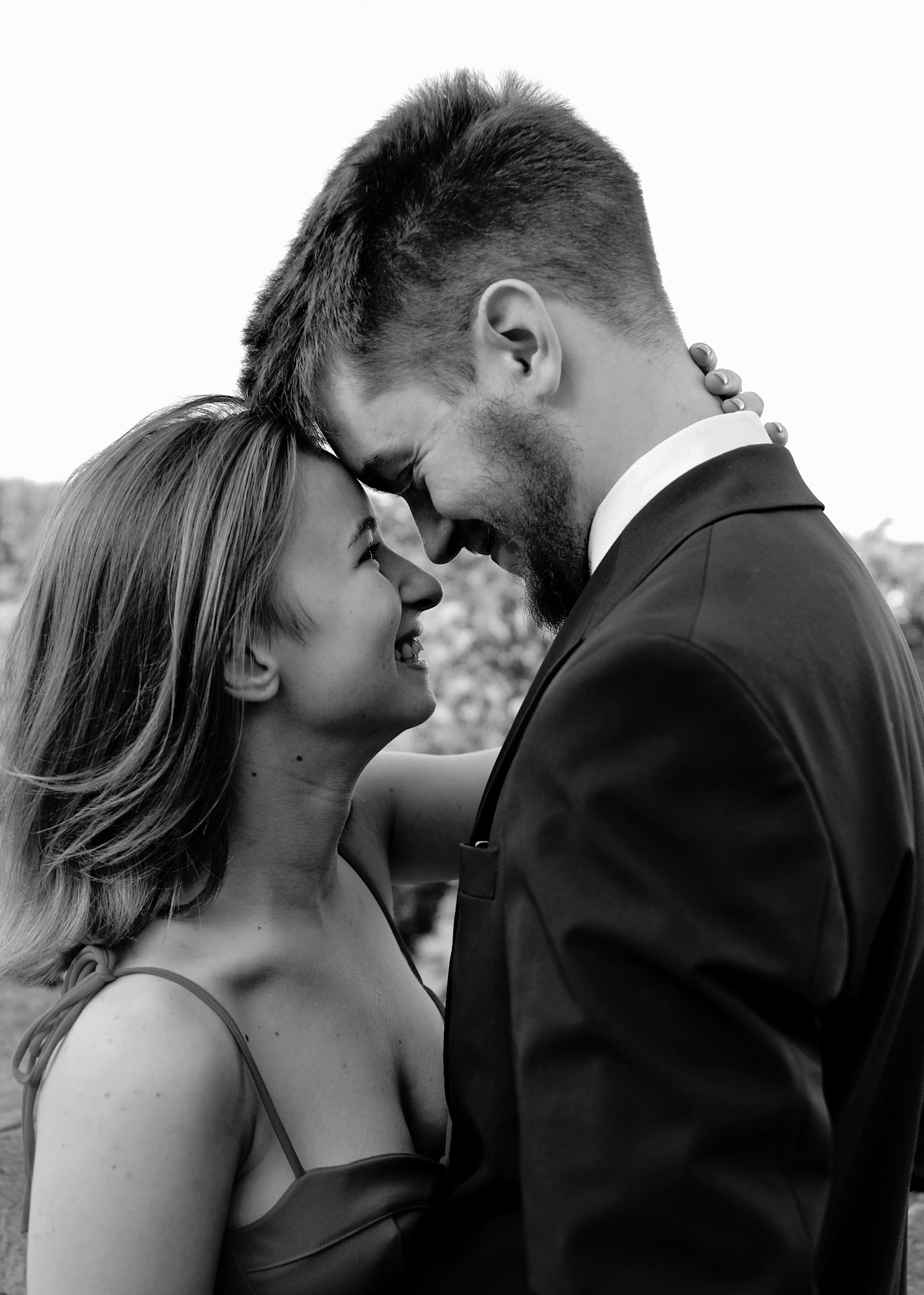 Czarno-białe zbliżenie uśmiechniętej pary: kobieta w sukience na ramiączkach i mężczyzna w garniturze dotykają się czołami.