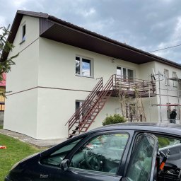 ComplexTerm - Dwupiętrowy dom po tynkowaniu elewacji, widoczne rusztowania i otwarty samochód z narzędziami przed domem, pochmurne niebo.