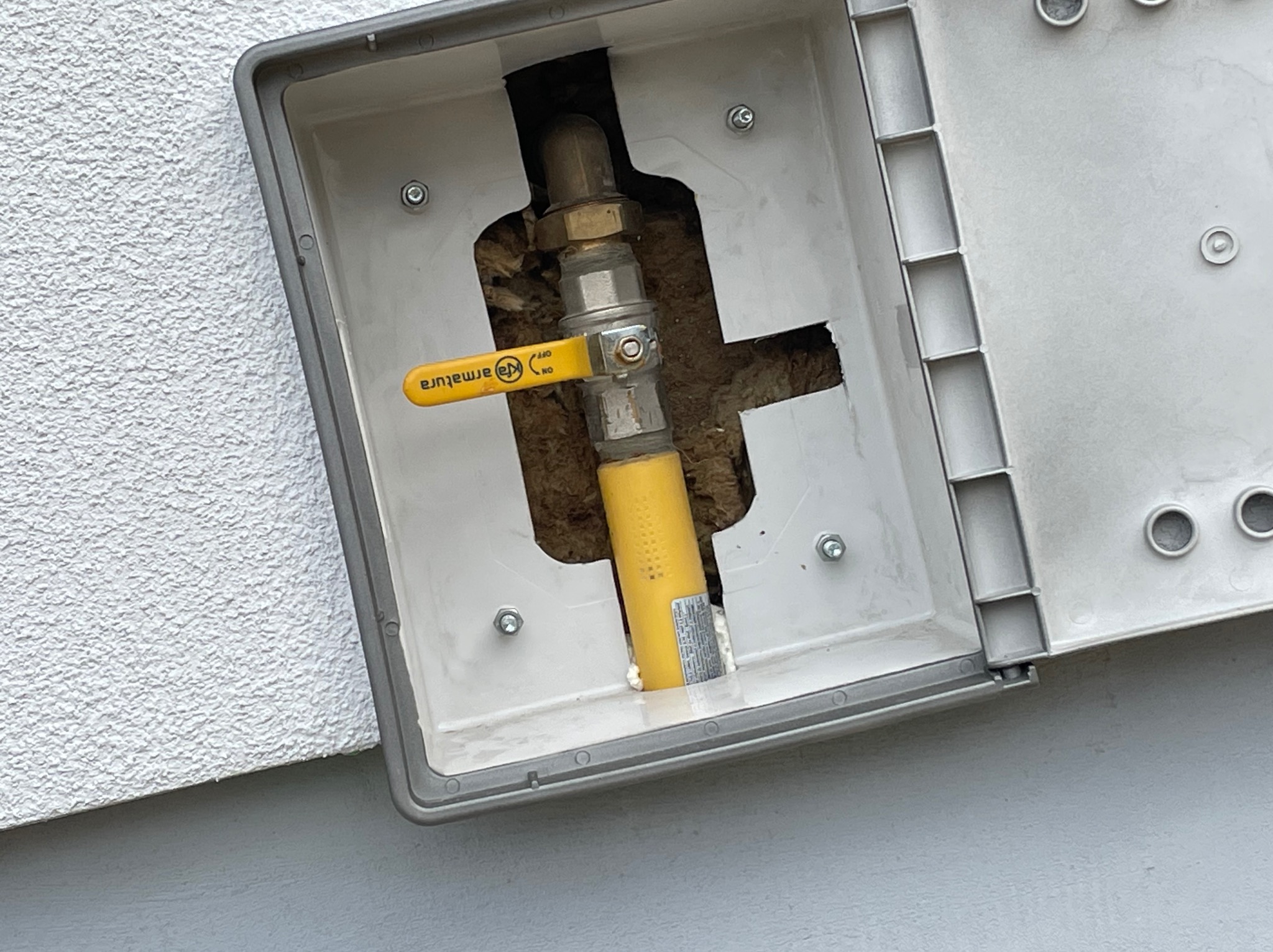 Żółty gazowy zawór odcinający Armatura w szarej skrzynce na elewacji budynku o chropowatej strukturze.