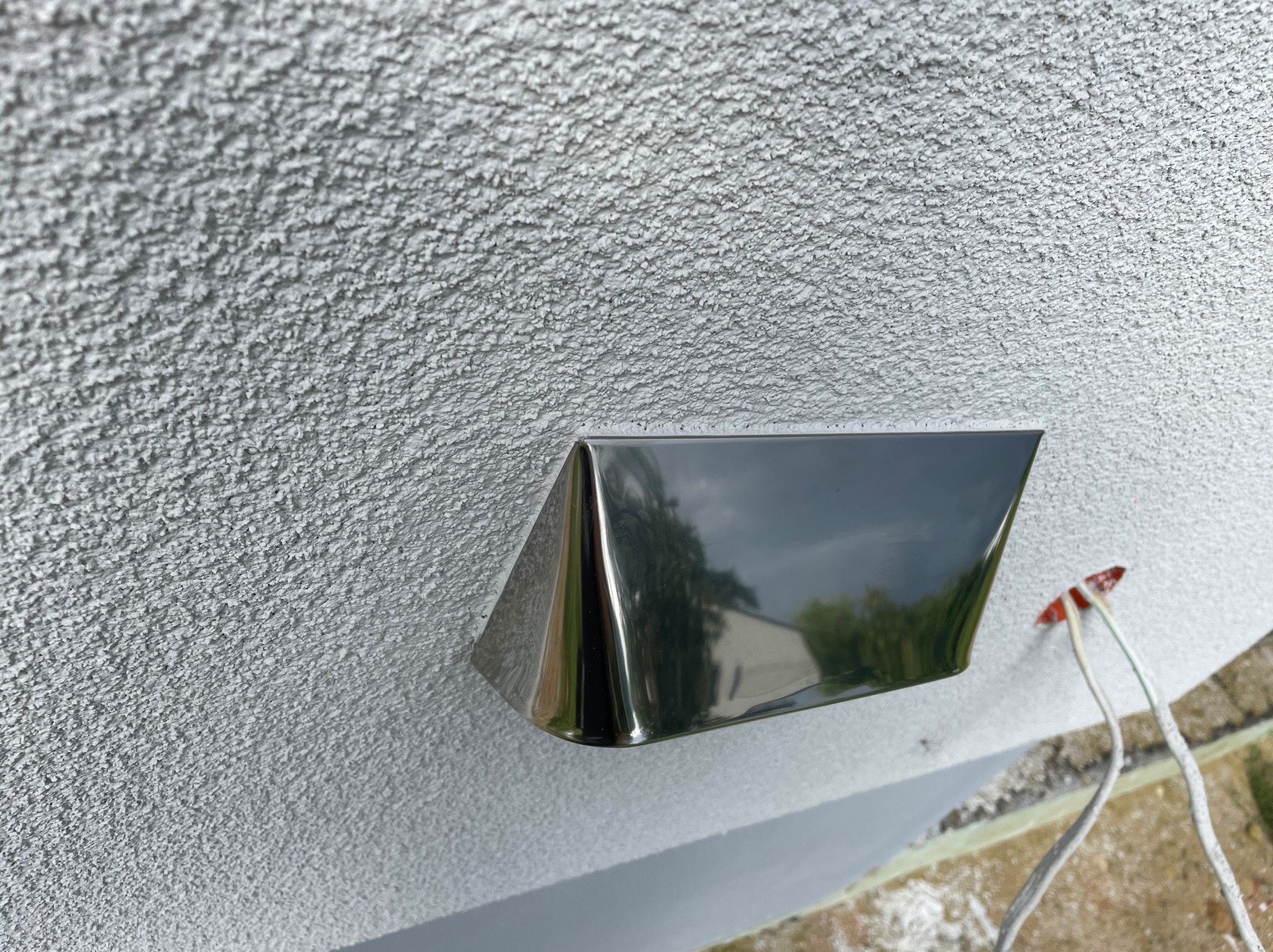 Szara elewacja z barankiem, metalowa obudowa oświetlenia zewnętrznego z widocznymi przewodami elektrycznymi.