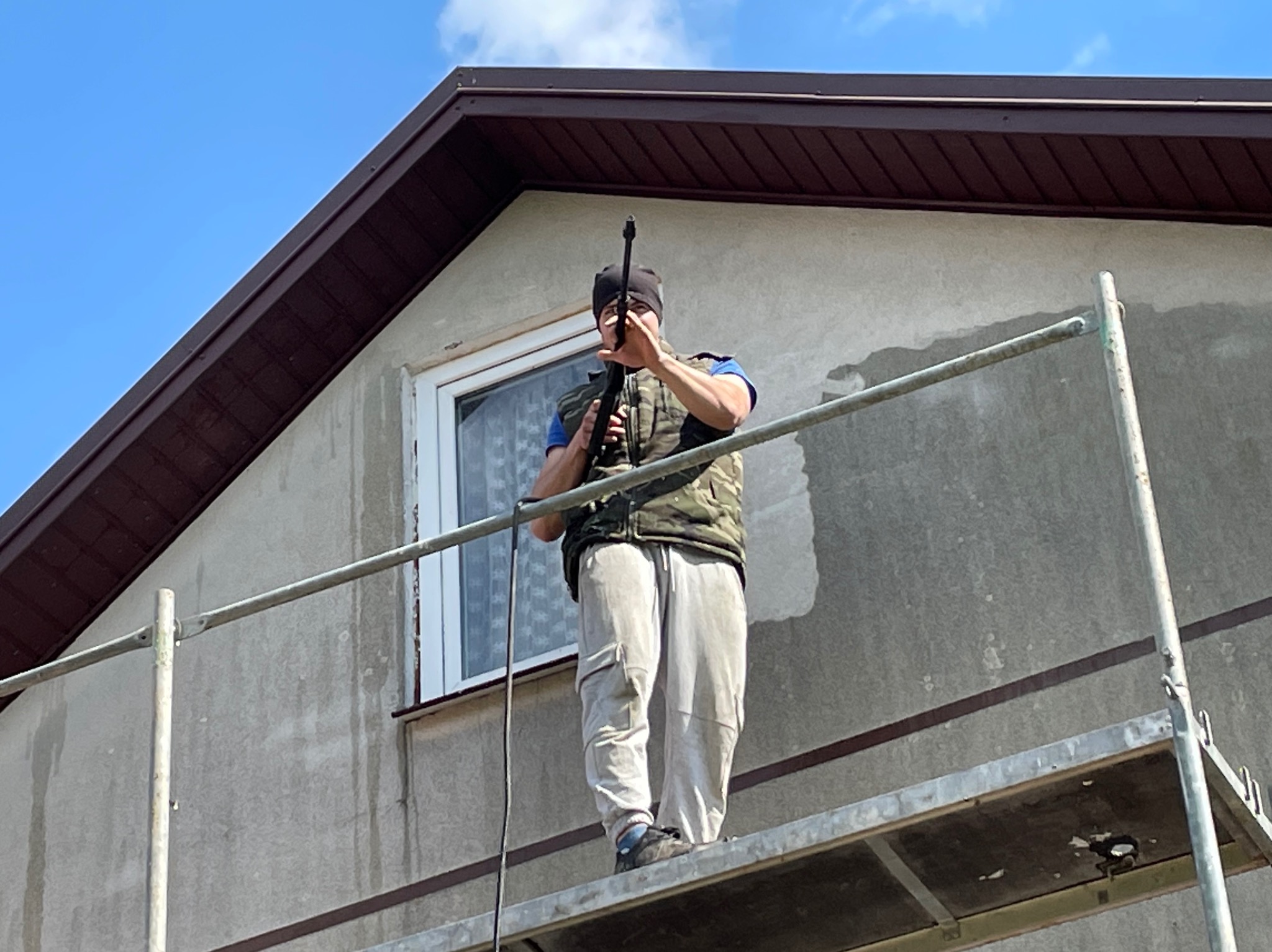 Pracownik na rusztowaniu czyści elewację domu za pomocą myjki ciśnieniowej, przygotowując ją do dalszych prac wykończeniowych.