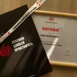 Certyfikat ukończenia szkolenia z przygotowania motorycznego dla Jakuba Wojciechowskiego, umieszczony w ramce, leżący obok czarnej teczki z logo Centrum Szkoleń Sportowych oraz smyczy z hasłem '...