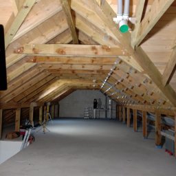 Extrem - Surowe poddasze z drewnianą konstrukcją dachu, widoczne instalacje wentylacyjne i przygotowane podłoże. W tle drabina i narzędzia.