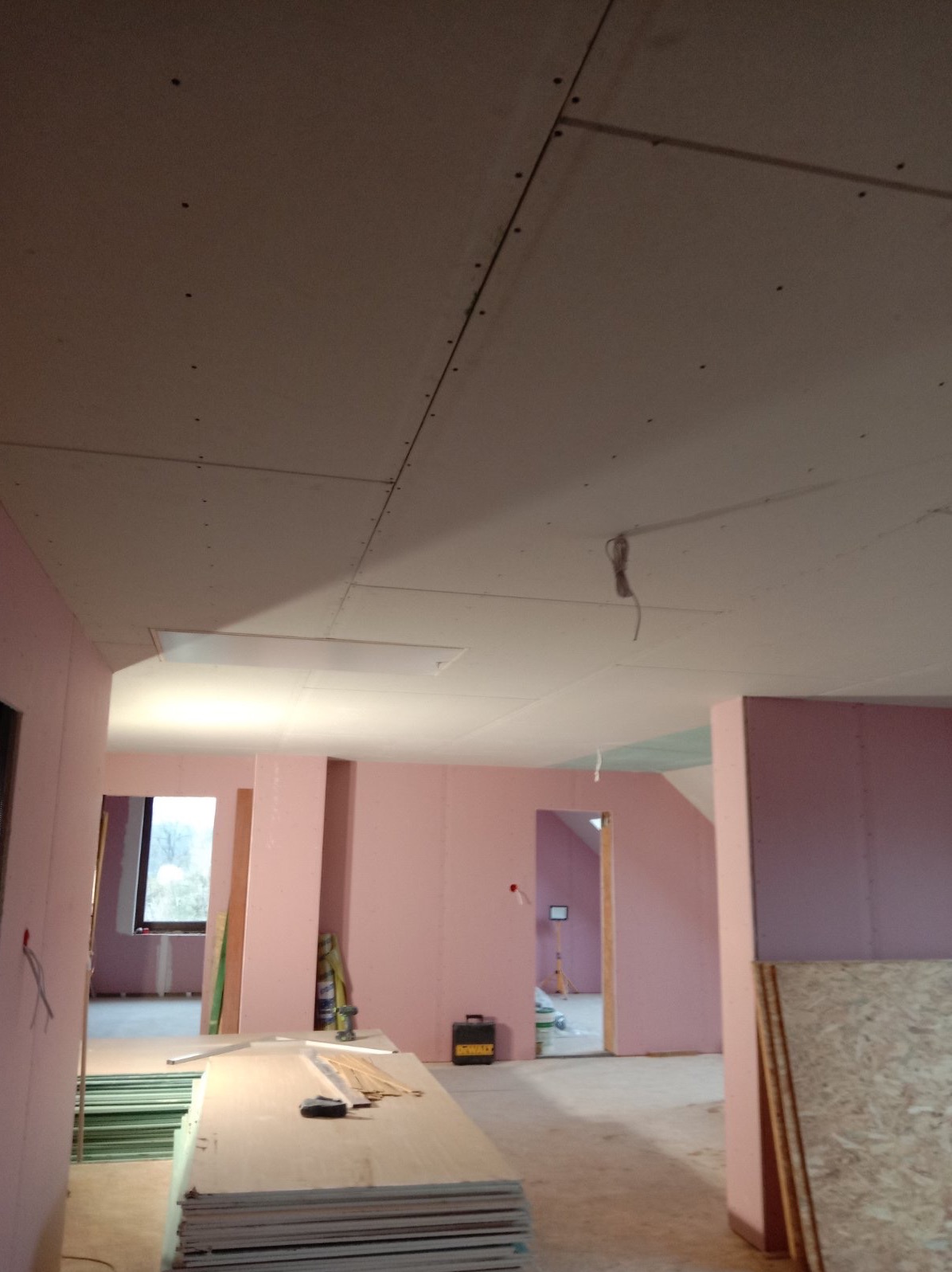 Poddasze w trakcie ocieplania: widoczne płyty izolacyjne koloru różowego na ścianach, sufity z płyt kartonowo-gipsowych, przygotowane materiały budowlane i narzędzia DeWalt.