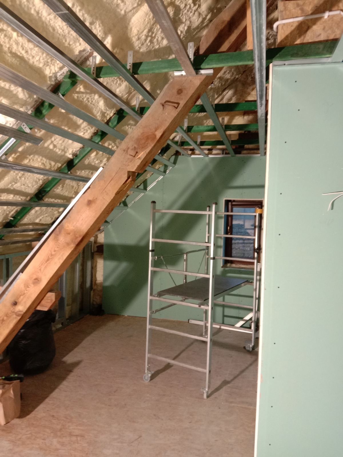 Poddasze w trakcie adaptacji: ocieplenie pianą, metalowa konstrukcja nośna, częściowo obłożone płytami gipsowo-kartonowymi, widoczne rusztowanie.