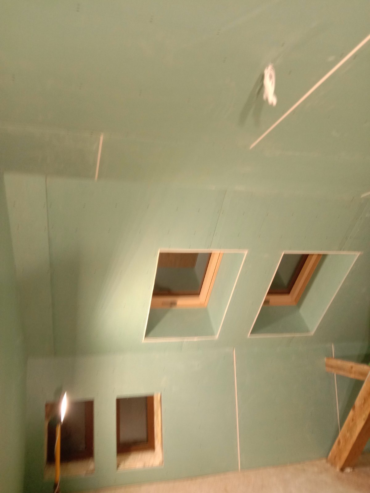 Poddasze z oknami dachowymi w trakcie montażu płyt gipsowo-kartonowych, widoczne łączenia płyt i konstrukcja okien.