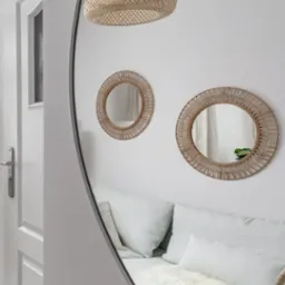 Okrągłe lustro odbija wnętrze: sofa z poduszkami i futrzanym pledem, dwa małe lustra na ścianie i pleciona lampa sufitowa, widoczny fragment białych drzwi.