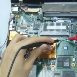 Multimetr Mastech podczas diagnostyki płyty głównej otwartego laptopa, widoczne ręce technika przykładające sondy do układu scalonego.