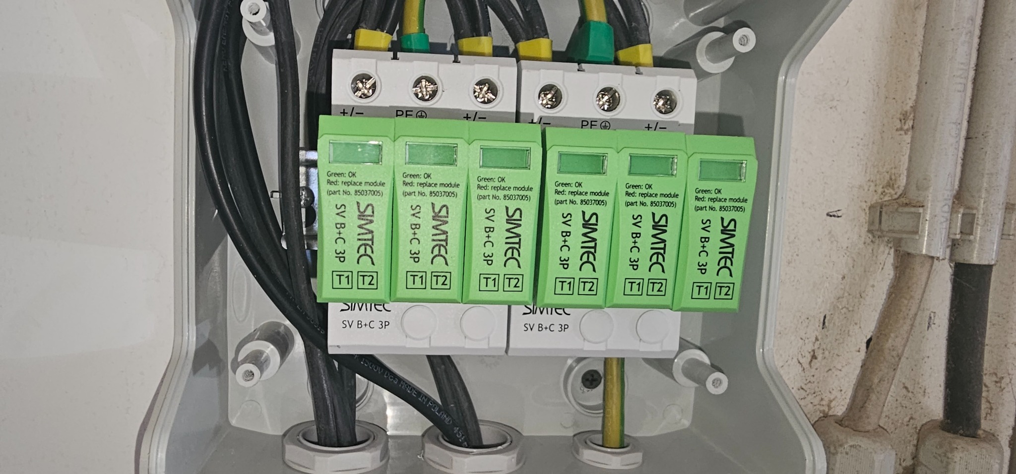 Wnętrze skrzynki elektrycznej z zamontowanymi modułami ograniczników przepięć marki Simtec SV B+C 3P, widoczne przewody w izolacji czarnej, żółto-zielonej i żółtej.