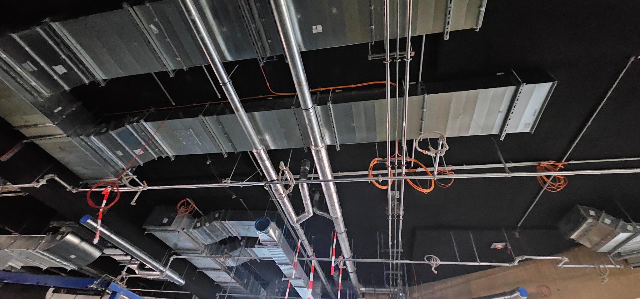 Widok sufitu technicznego z licznymi rurami, kanałami wentylacyjnymi i przewodami elektrycznymi, w tle ciemna przestrzeń sufitu podwieszanego.