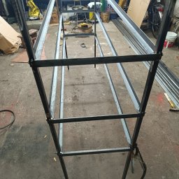 Patryk czwójdak - Metalowa konstrukcja szkieletowa, prawdopodobnie w trakcie spawania, widoczne spawy, w warsztatowym otoczeniu z narzędziami i materiałami.