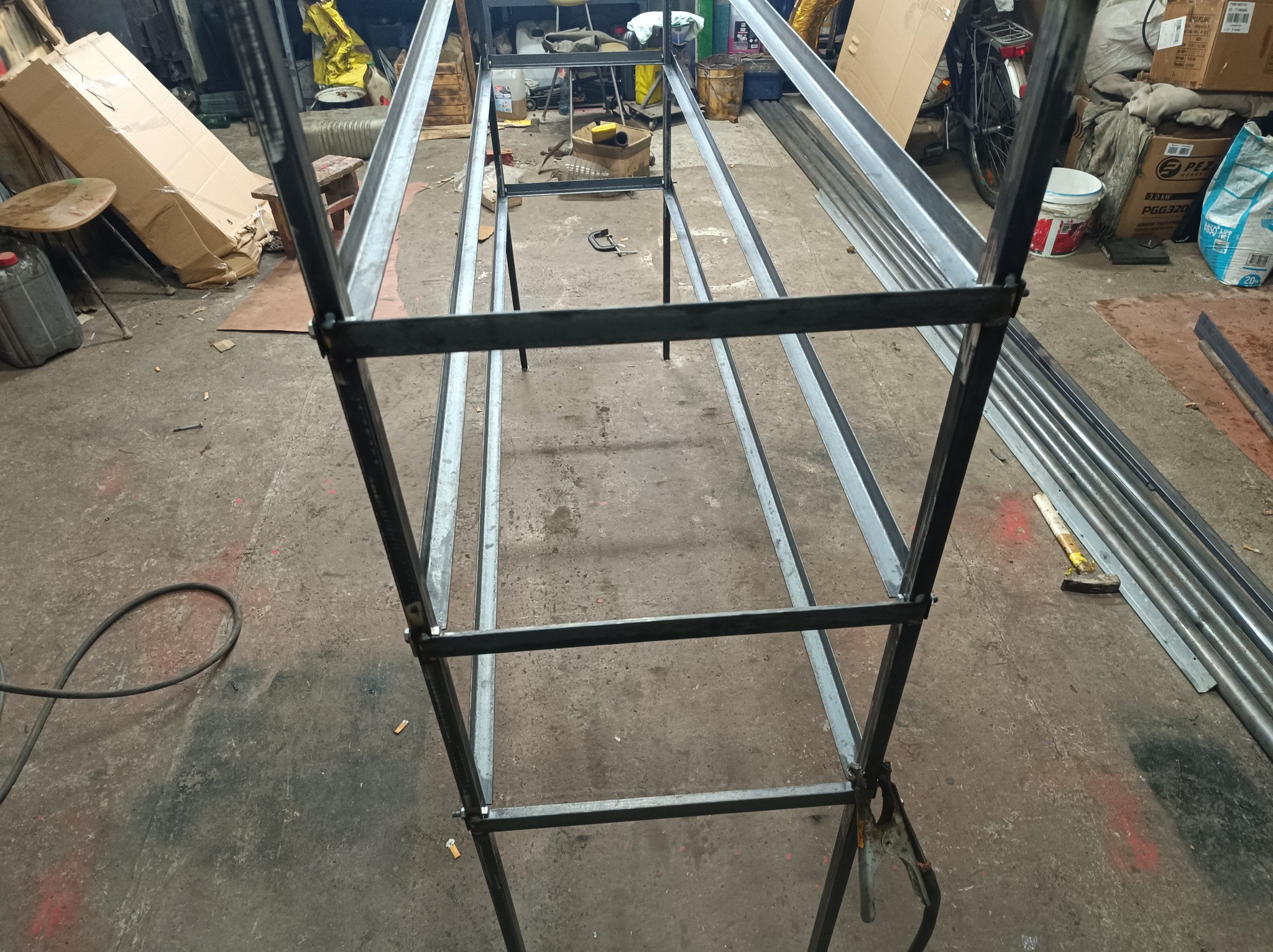 Metalowa konstrukcja szkieletowa, prawdopodobnie w trakcie spawania, widoczne spawy, w warsztatowym otoczeniu z narzędziami i materiałami.