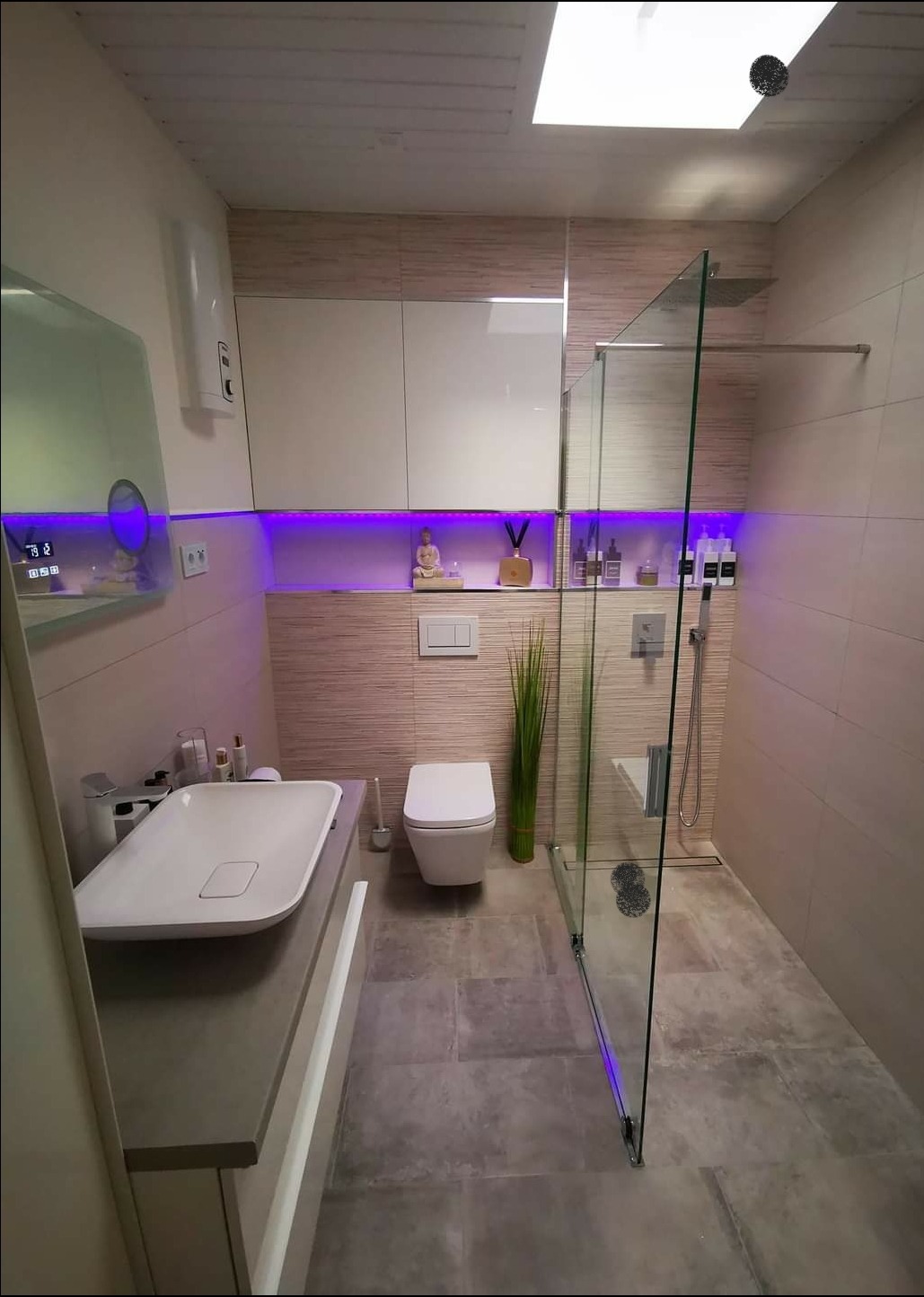 Nowoczesna łazienka z podświetleniem LED, kabiną prysznicową ze szkła, umywalką nablatową i toaletą wiszącą, wykończona w beżowych płytkach imitujących drewno.