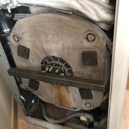 Paweł Roliński ROL-FIX - Wnętrze pralki automatycznej w Łodzi. Widoczny betonowy obciążnik bębna z zamocowanymi elementami metalowymi i śladami użytkowania.