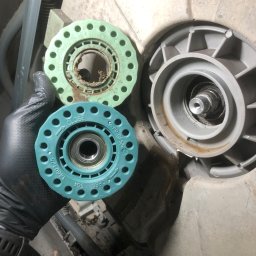 Paweł Roliński ROL-FIX - Ręka w rękawicy trzyma zużyty element zmywarki, obok widoczny drugi, zamontowany element. Widoczne ślady użytkowania i zabrudzenia.